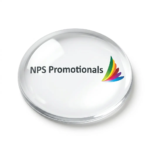 Custom glass dome paperweight resting on a wooden office desk, displaying a full-colour printed logo visible through the clear dome.