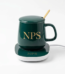 Dark green ceramic mug with a matching lid and gold spoon resting on an electric heating coaster, featuring custom logo printing.